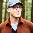 A photo of a man wearing a hat and glasses with trees in the background.